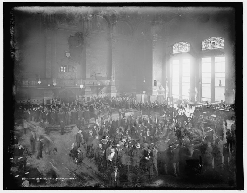 A large hall of the Chicago Board of Trade during a session, photographed from a gallery: hundreds of men crowded on the floor, tall windows letting in light.